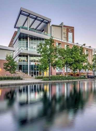 A modern building with a glass facade is reflected in the water in front of it.