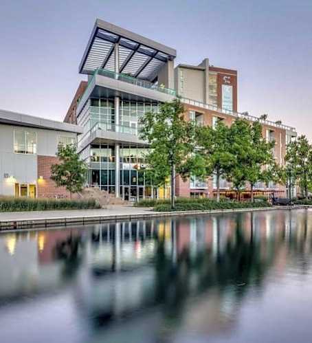 A modern building with a glass facade is reflected in the water in front of it.