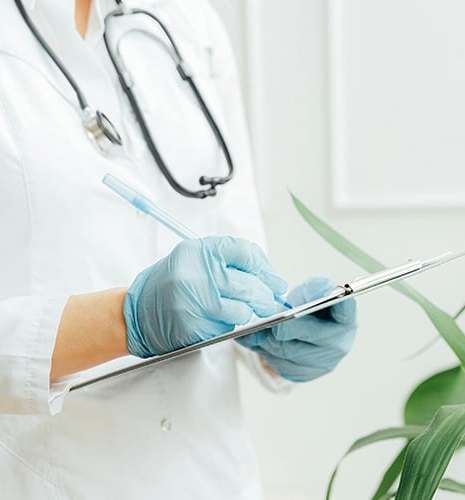A person in a white coat and blue gloves holds a clipboard.