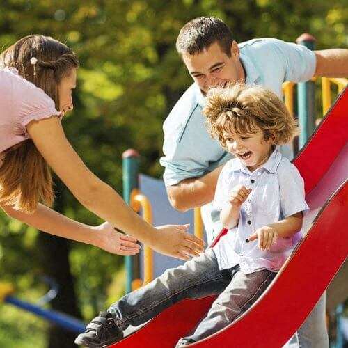 A child slides down a red slide at a playground.