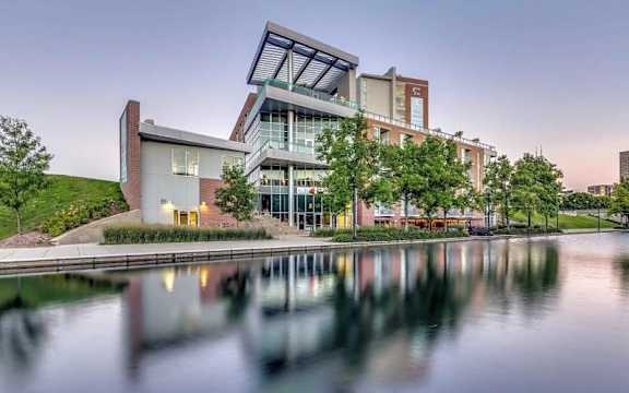 A modern building with a glass facade is reflected in the water in front of it.