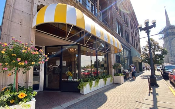 a city street with people walking and a building with a yellow and white awning