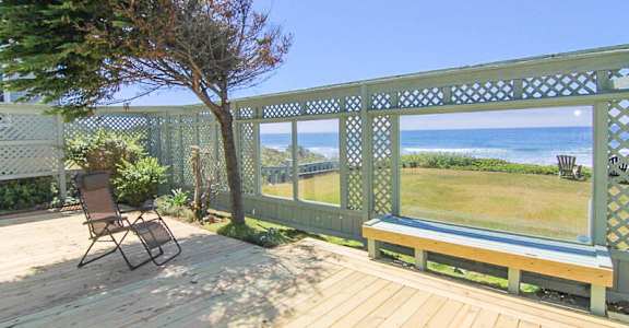 A wooden deck with a bench and a chair overlooking the ocean.
