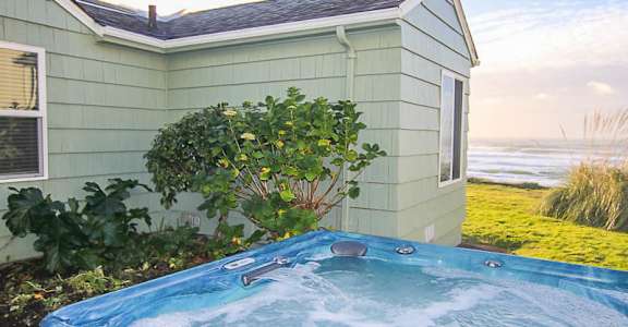 A hot tub sits in front of a house with a green lawn.