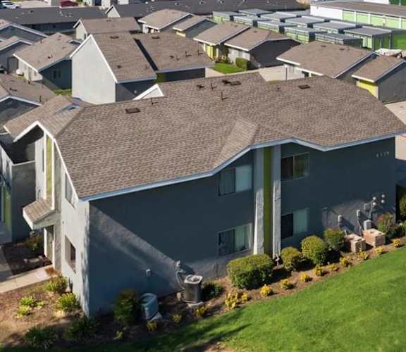 A large grey house with a brown roof and a green lawn in front.