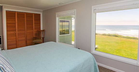 A bedroom with a bed, a chair, and a view of the ocean through a window.