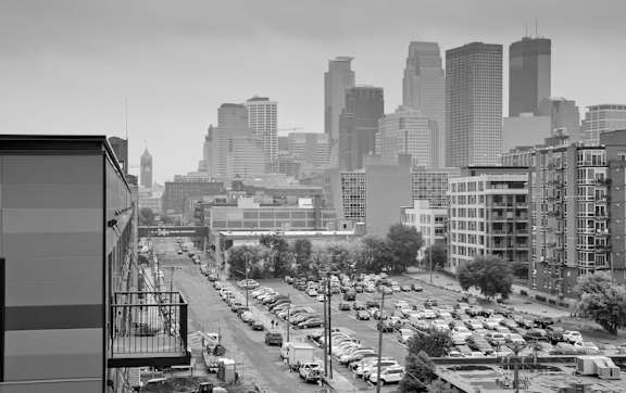 A black and white image of a city street with cars and buildings.