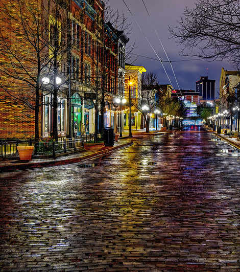 A cobblestone street at night with lights from the buildings.