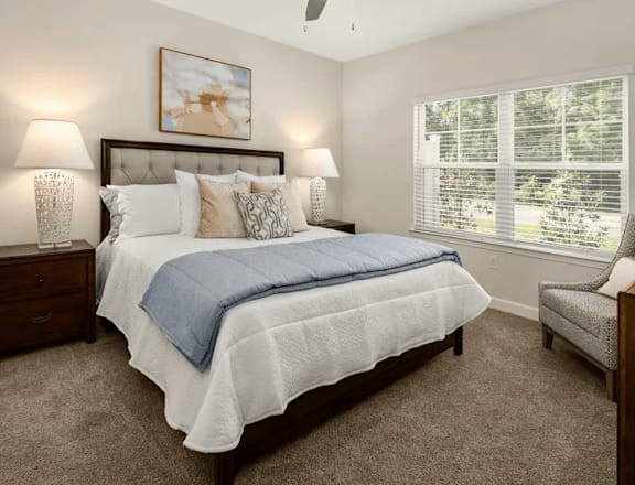 A bedroom with a bed, two lamps, a painting, and a window.