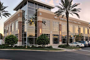 An exterior view of the Gainesville Health & Fitness Center with palm trees and a parking lot near The Flats at Tioga Town Center apartments.