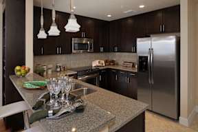 An updated kitchen with stainless steel appliances, granite countertops, recessed lighting, modern pendant lights, and a double-basin sink.
