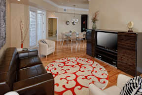 A staged living room with hardwood-style flooring and double door access to a private balcony near a kitchen.