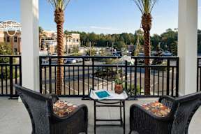 A beautiful private covered balcony with two wicker chairs and a small table with beautiful views of Tioga Town Center, ample parking, and large trees.