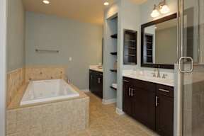 A large bathroom with a bathtub, a walk-in shower, and 2 separate vanity sinks divided by built-in shelving.