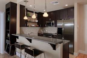 A modern kitchen with dark cabinets, stainless steel appliances, a breakfast bar with pendant lights, and built-in open shelves.