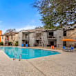A swimming pool surrounded by a concrete floor and a fence with a building in the background.