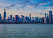 Thumbnail 3 of 8 - A city skyline with tall buildings and a body of water in the foreground.