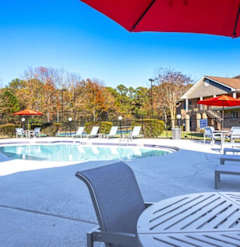 A pool with a red umbrella and lounge chairs.