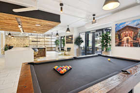 A pool table is in the middle of a room with a ceiling fan and a painting on the wall.