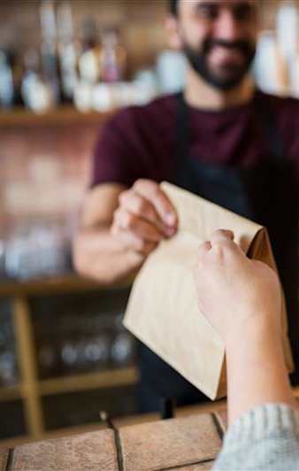 A person in a maroon shirt is handing a brown paper bag to another person.