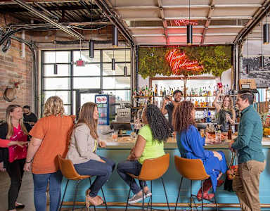 A group of people are sitting at a bar with a neon sign in the background.
