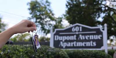 A person holding keys in front of a Dupont Avenue Apartments sign.