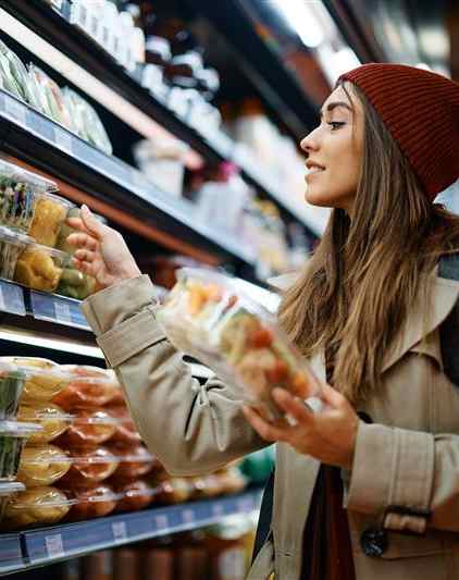 A woman in a beanie is shopping for vegetables in a grocery store.