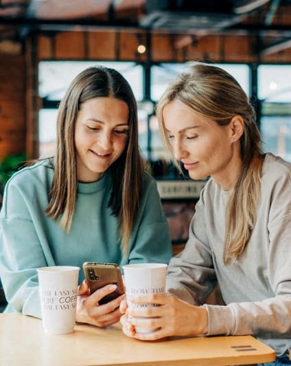 Lifestyle photo of two women looking at a cellphone over coffee