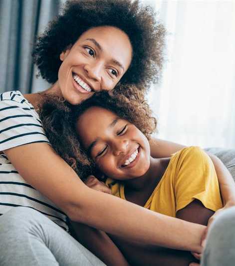 A woman with a striped shirt is hugging a child on a grey couch.