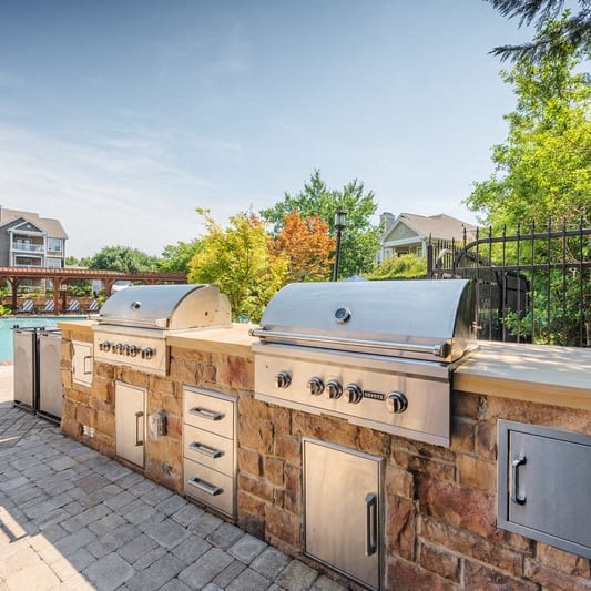 an outdoor kitchen with two grills and a swimming pool