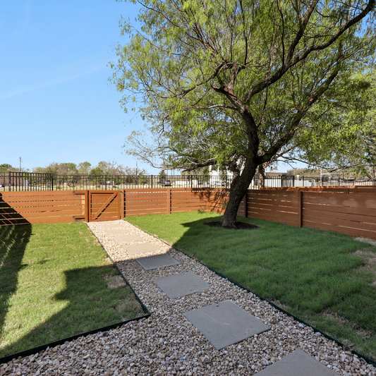 A backyard with a gravel path and a tree.
