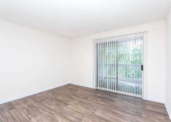 A room with a sliding glass door and wooden flooring.