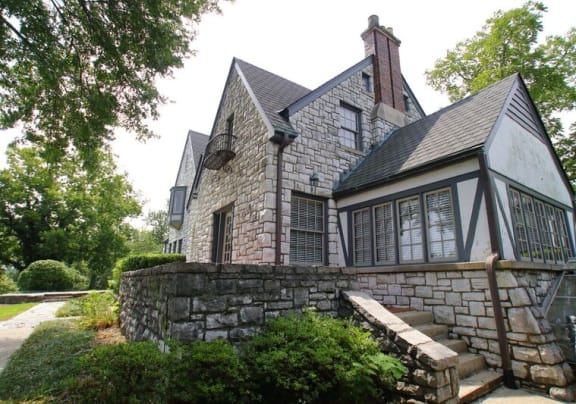 a stone house with a gray roof and a stone wall in front of it