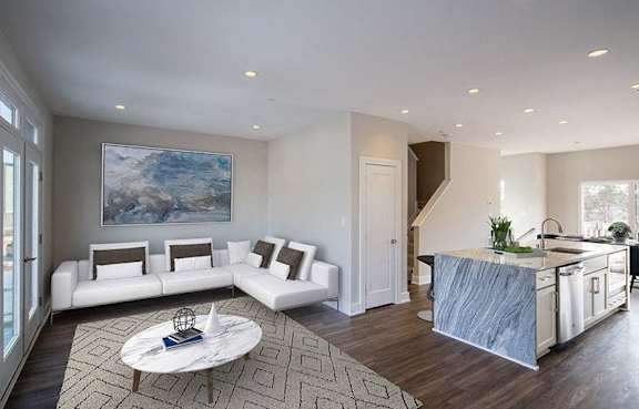 A modern living room with a large painting on the wall and a marble countertop kitchen.