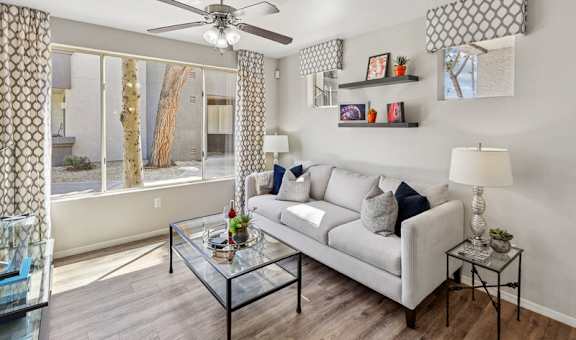 A living room with a grey couch, a glass coffee table, and a ceiling fan.