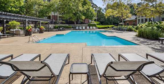 A pool surrounded by lounge chairs and trees.