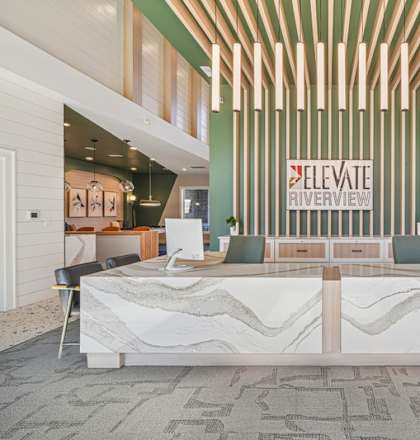 A reception area with a white reception desk and a green wall with a sign that says "Elevate Riverview".