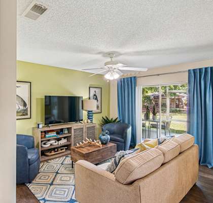 A living room with a blue couch, a television, and a fan.