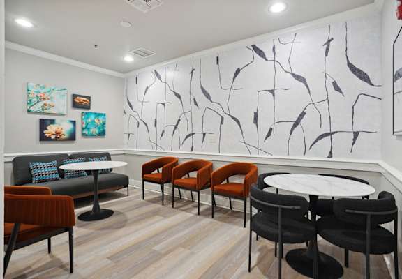 a seating area with tables and chairs in a room with a painting on the wall