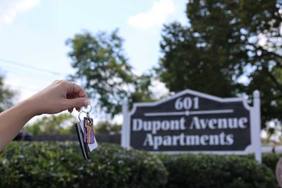A person holding keys in front of a Dupont Avenue Apartments sign.