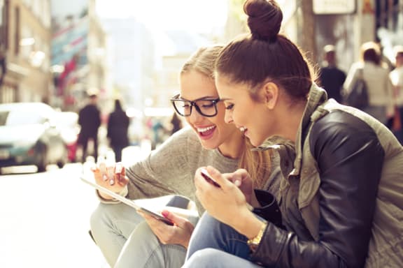two women sitting on a bench looking at an Ipad