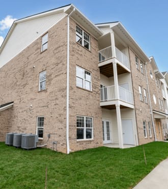 a brick apartment building with green grass and a sidewalk