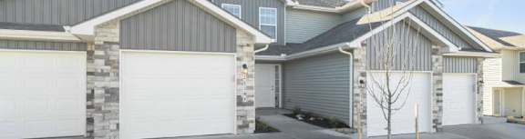 A row of houses with garages and a small tree in the front yard.