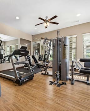 One-Bedroom Apartments In Lawrence, KS - Camson Place - A Modern Fitness Center With Wood-Style Flooring, A Large Wall Mirror, A Treadmill, An Elliptical, And A Multi-Station Weight Machine.
