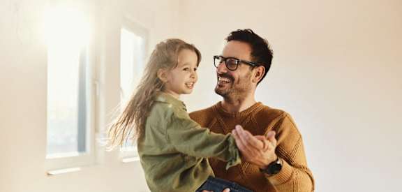 Lifestyle photo of a man and his daughter dancing and smiling in the living room