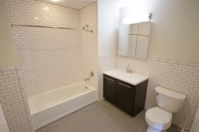 bathroom with dark wooden cabinets, grey laminate floors and white tiled walls