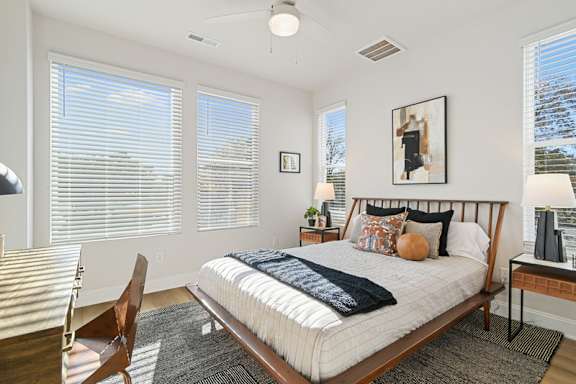 A bedroom with a bed, chair, and window with blinds.