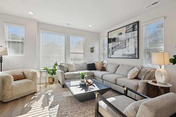 A well-lit living room with a grey sofa, a glass coffee table, and a large artwork on the wall.