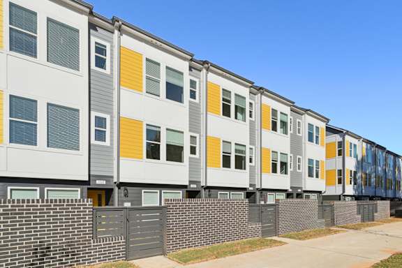 A row of modern townhouses with grey, white, and yellow exterior panels.
