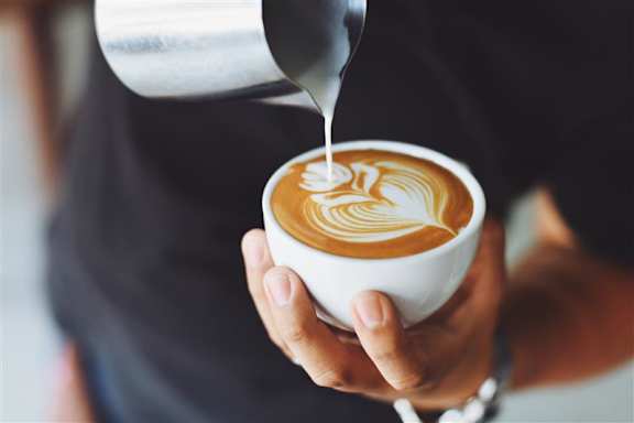 A person is pouring milk into a cup of coffee.